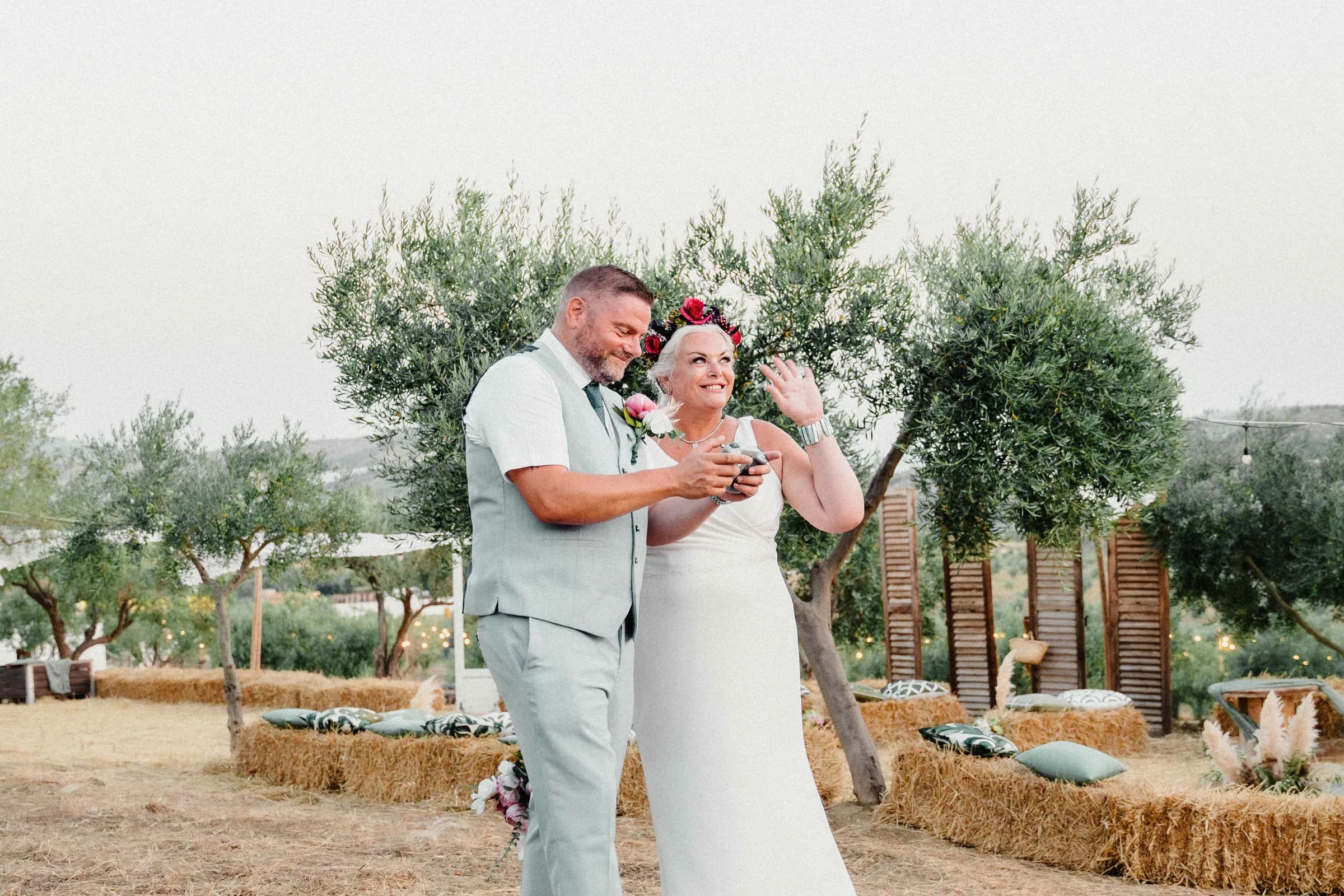 The couple opening a bottle together among the olive trees, laughing