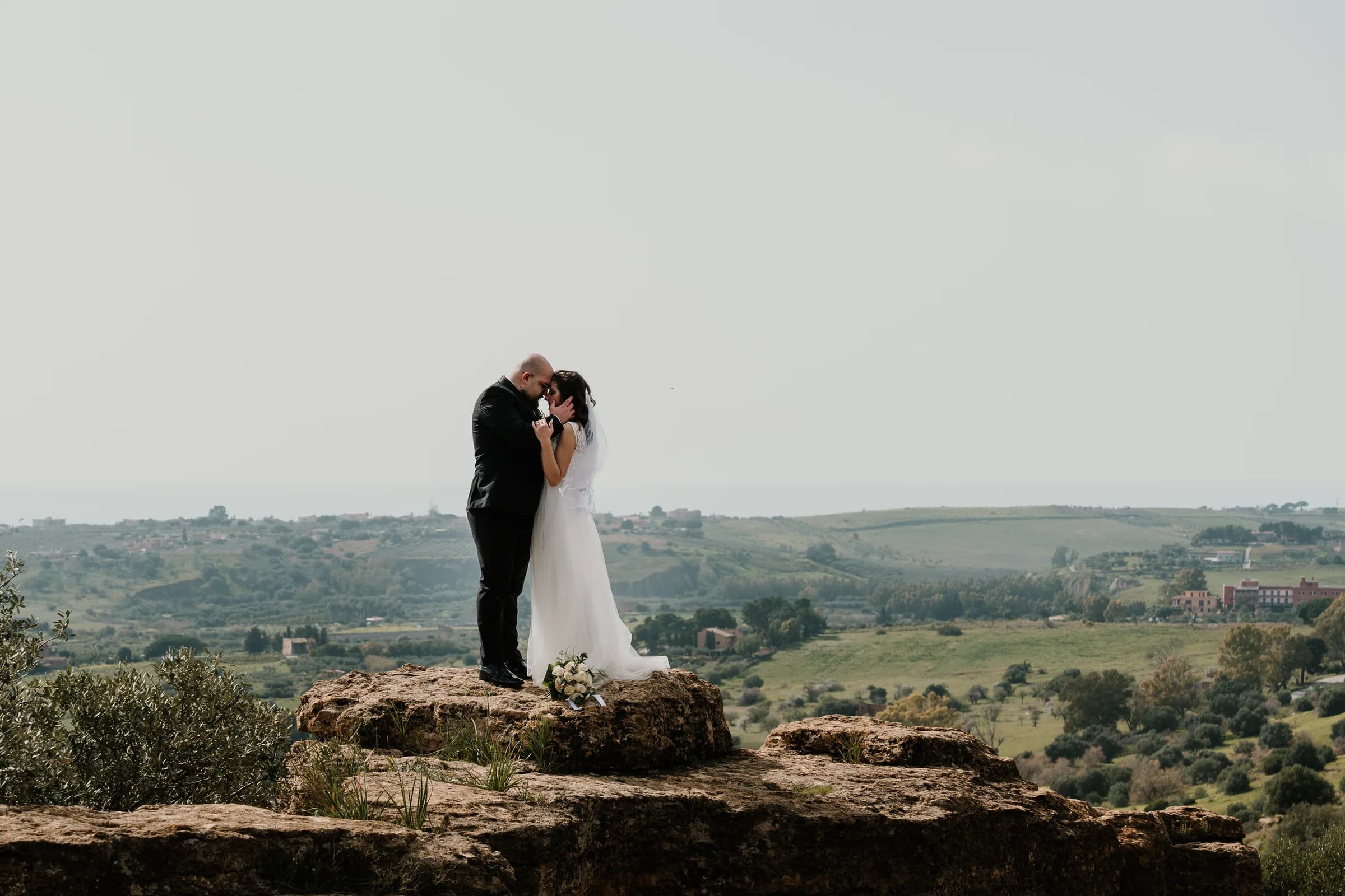 A couple kissing on a stone ridge, olive country beyond